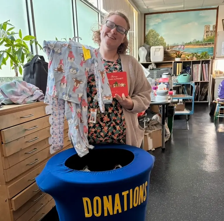 Pine View teacher with donated holiday pajamas and a book at the donations bin