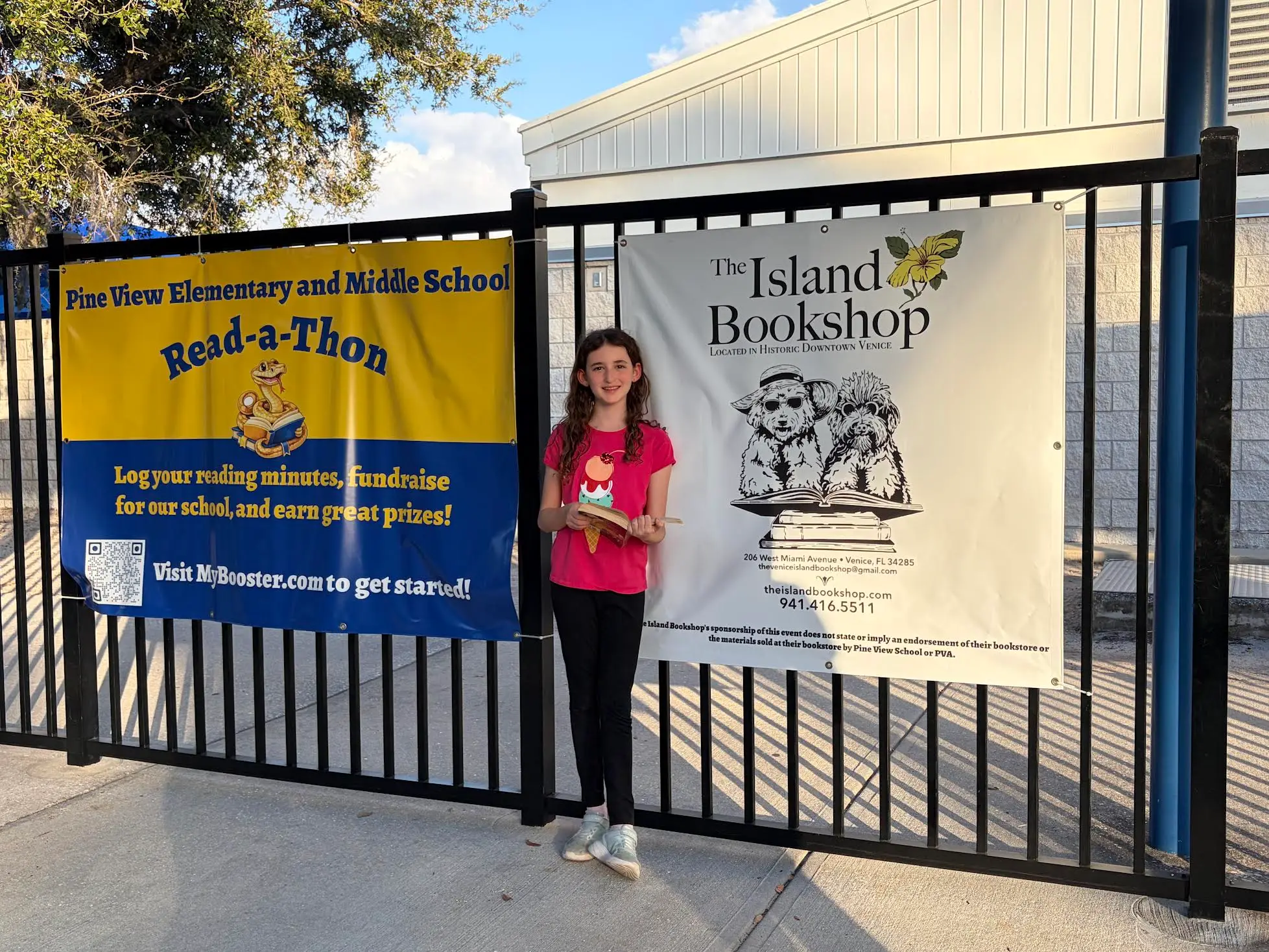 Samantha Wagner holding a book in front of the Read-a-thon and Island Bookshop banners